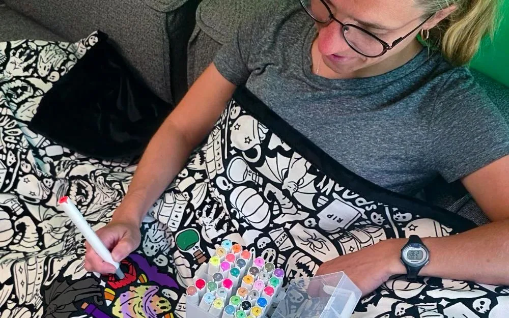 Coloring Your Own founder Michelle Mildred coloring one of her black-and-white blankets with markers